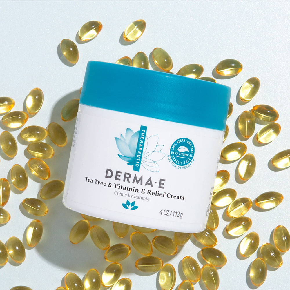 Derma E Tea Tree and Vitamin E Relief Cream container surrounded by Vitamin E capsules.