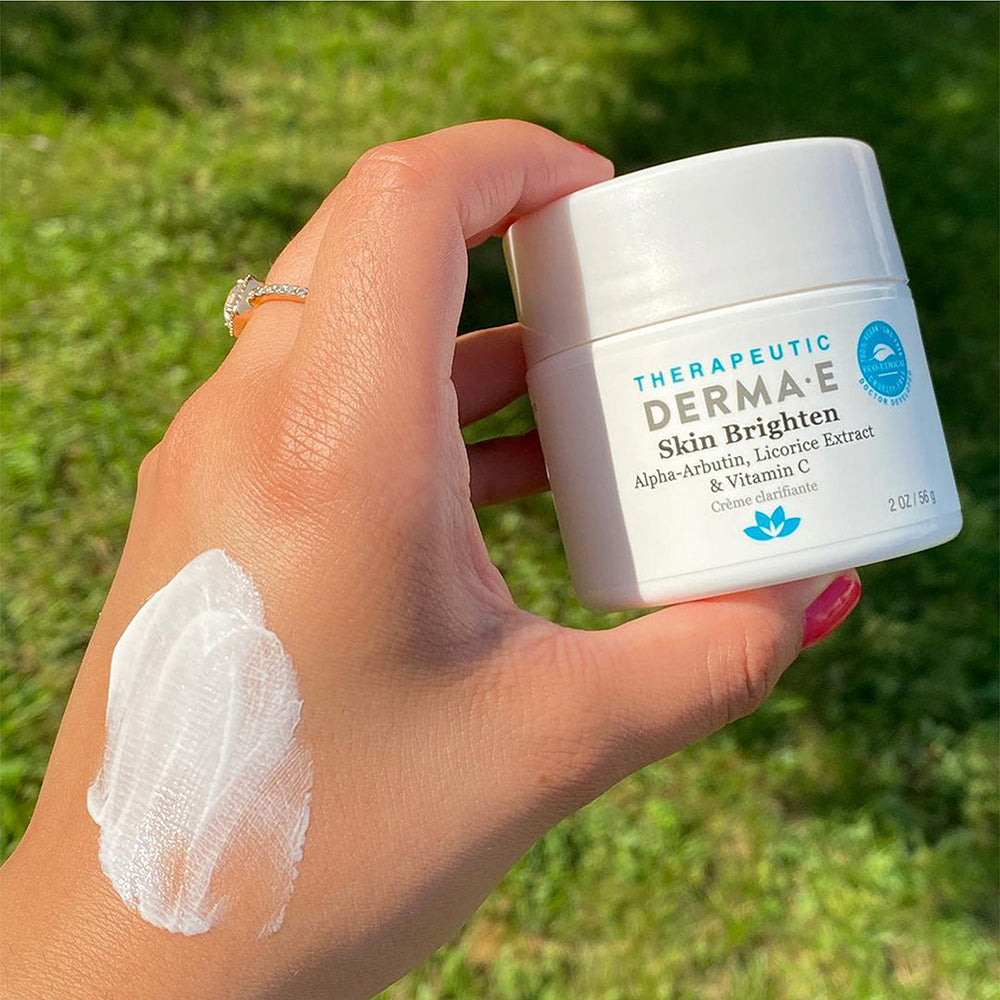 A hand holding a jar of skin brighten with a smear of their hand.
