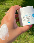 A hand holding a jar of skin brighten with a smear of their hand.
