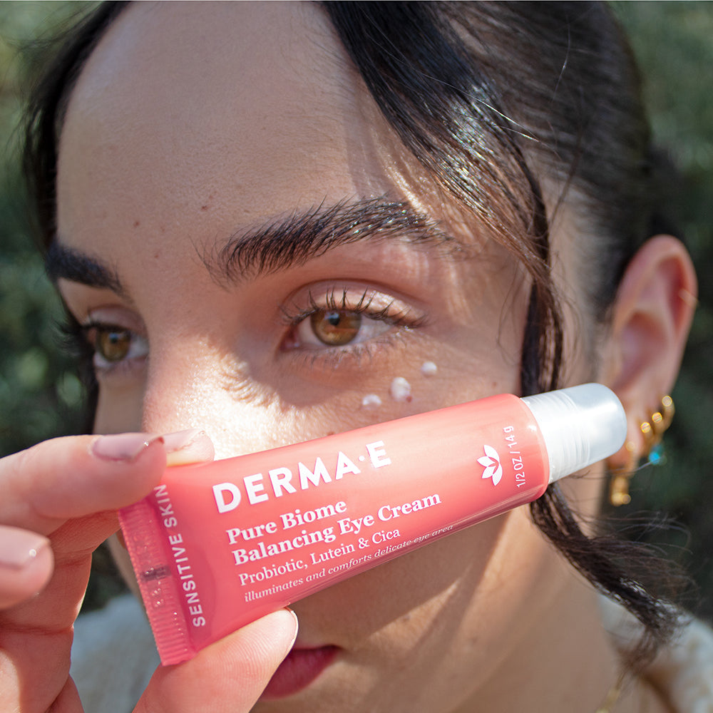 Woman holding a tube of Pure Biome Balancing Eye Cream with products under her eye.