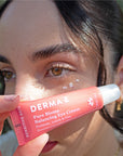 Woman holding a tube of Pure Biome Balancing Eye Cream with products under her eye.