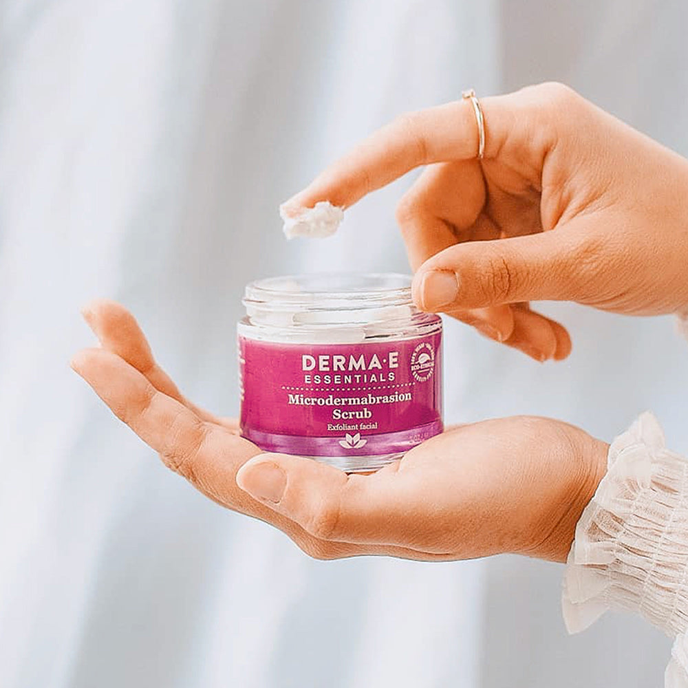 Hands holding and applying Derma E Essentials Microdermabrasion Scrub, showcasing its creamy texture.