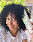 A women holds a tube of DERMA‑E 2‑in‑1 Curl Defining Crème next to their well‑defined curly hair. The focus is on the curls and the product, showcasing how the cream fits into a curl‑care routine and emphasizing its styling benefits.