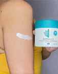 Woman holding Derma E's Tea Tree and Vitamin E Relief Cream jar with smear on her arm.