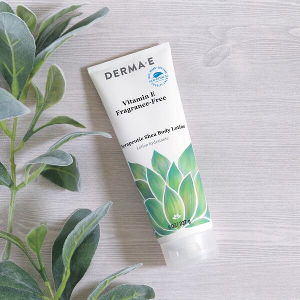 Flat lay of DERMA E Fragrance-Free Vitamin E Body Lotion with ingredients such as Aloe Vera, Chamomile, and Shea Butter