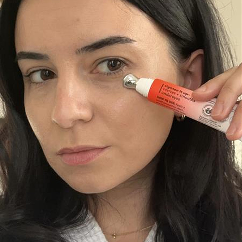 Woman applying a red and white tube of cream to her face.