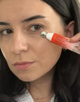 Woman applying a red and white tube of cream to her face.