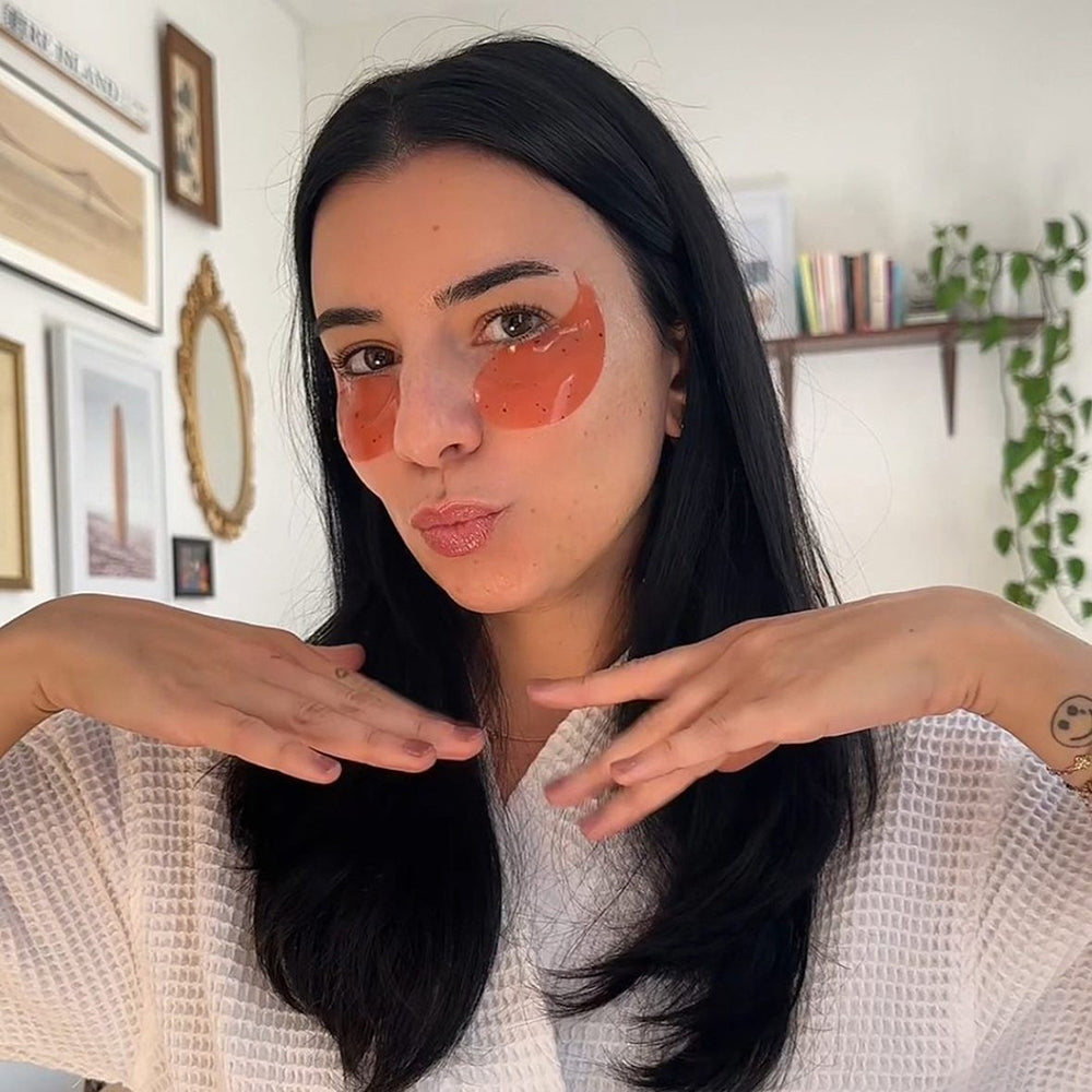 Woman with orange patches on her face pointing to them in a room with decor.