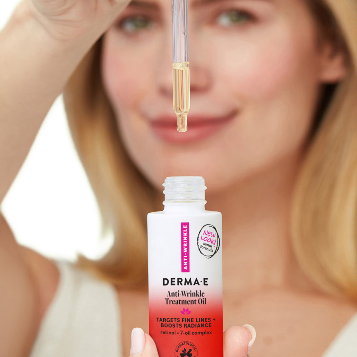 A woman holds a dropper above an open bottle of DERMA-E Anti Wrinkle Treatment Oil. The bottle is white with a red gradient base and pink vertical text, while the woman's face is softly blurred in the background.