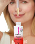A woman holds a dropper above an open bottle of DERMA-E Anti Wrinkle Treatment Oil. The bottle is white with a red gradient base and pink vertical text, while the woman's face is softly blurred in the background.