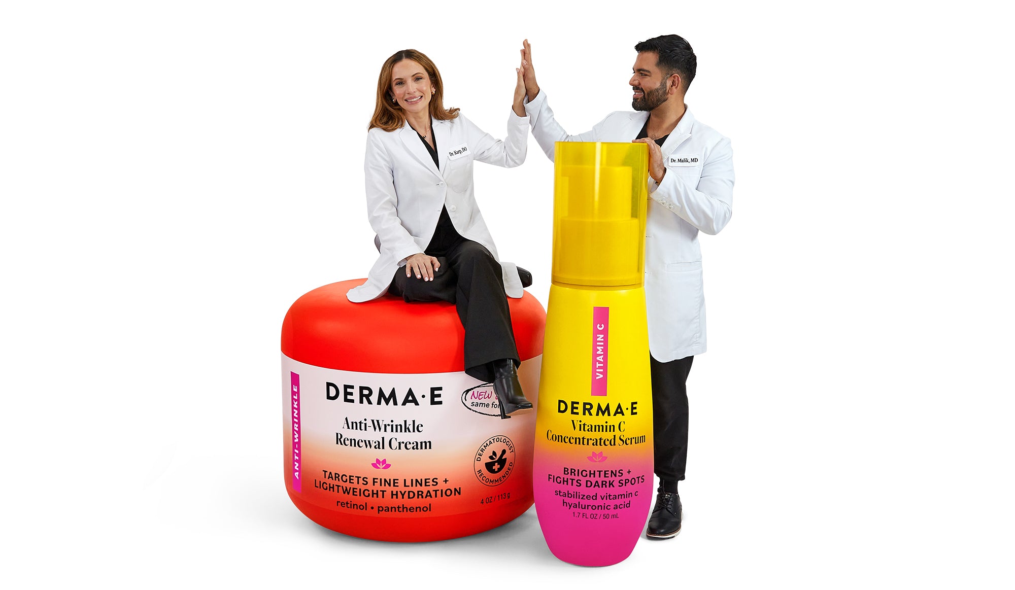 Two people sitting on large skincare product containers with a Derma E bottle in the foreground.