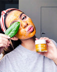 Woman using and holding a jar of Vitamin C Instant Radiance Citrus Facial Peel