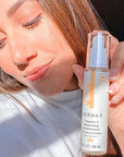 Smiling woman holding Derma E Vitamin C Renewing Moisturizer bottle near her face, highlighting the product's packaging and the natural glow of her skin.