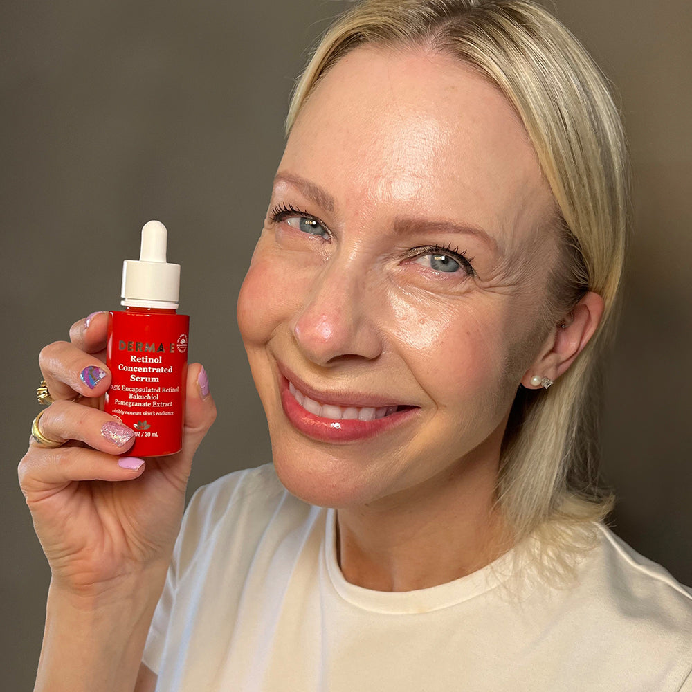 Smiling woman holding Derma E Retinol Concentrated Serum bottle, highlighting the product&#39;s packaging and her youthful skin.