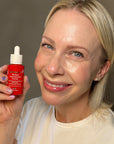 Smiling woman holding Derma E Retinol Concentrated Serum bottle, highlighting the product's packaging and her youthful skin.