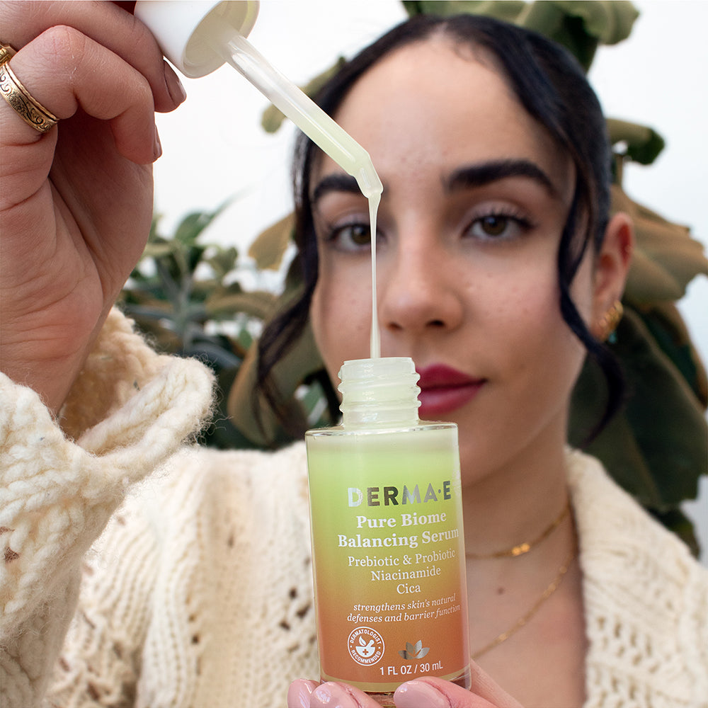 Woman holding a bottle of Pure Biome Balancing Serum and showing its texture. 