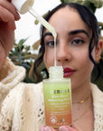 Woman holding a bottle of Pure Biome Balancing Serum and showing its texture. 