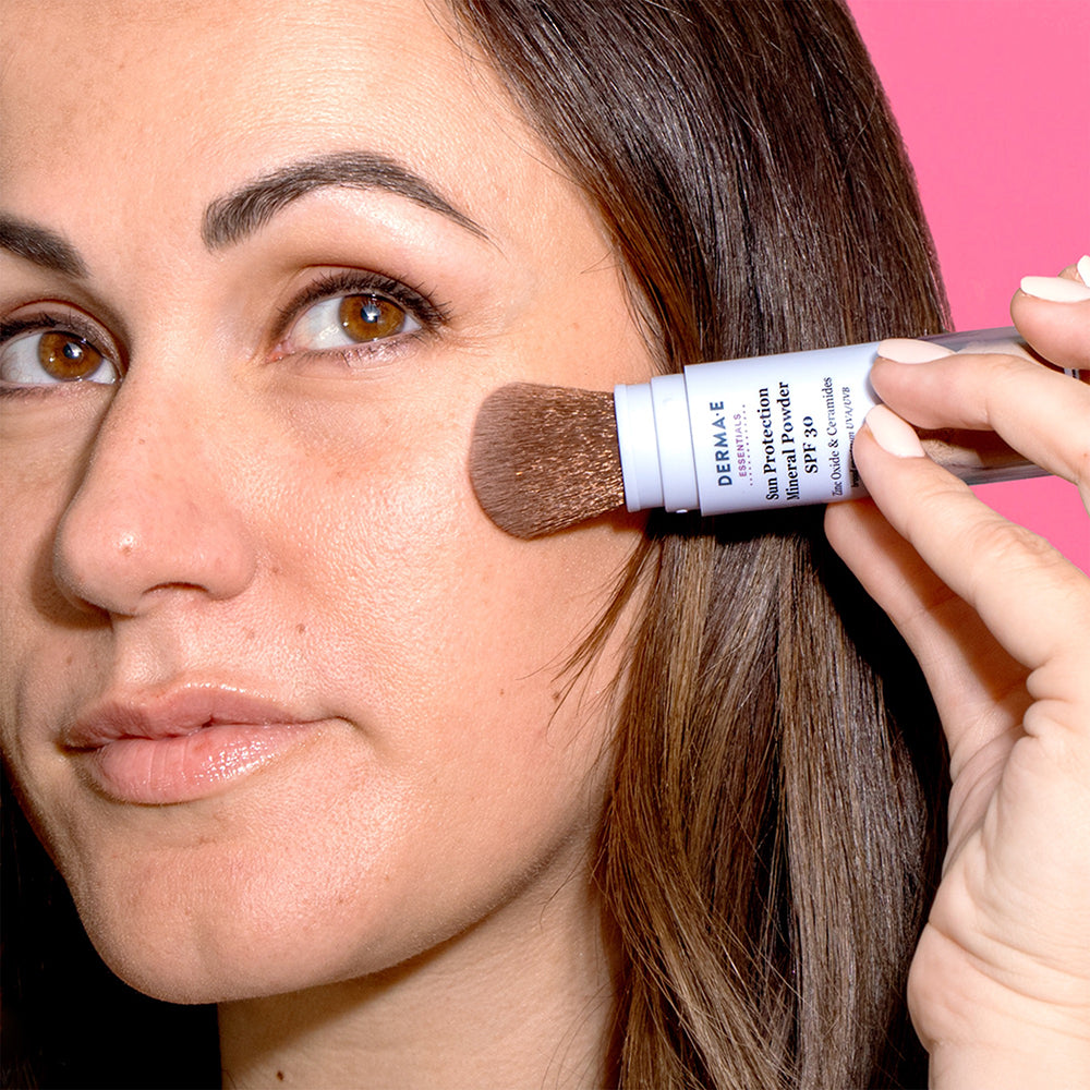 Woman applying Derma E Sun Protection Mineral Powder SPF 30 to her face, demonstrating easy and effective sun protection application.