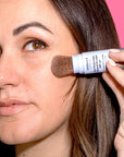 Woman applying Derma E Sun Protection Mineral Powder SPF 30 to her face, demonstrating easy and effective sun protection application.